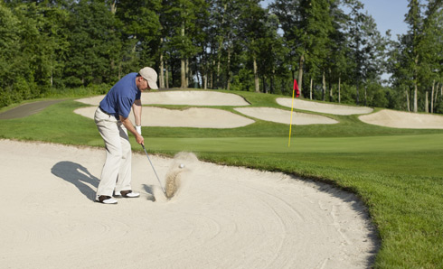 Man playing golf from bunker onto green